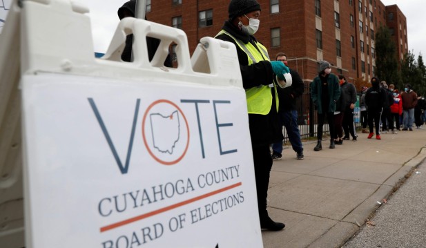 A poll worker stands on the curbside to collect drop-off votes as people wait in line to cast early in-person votes at the Cuyahoga County Board of Elections in Cleveland, Ohio